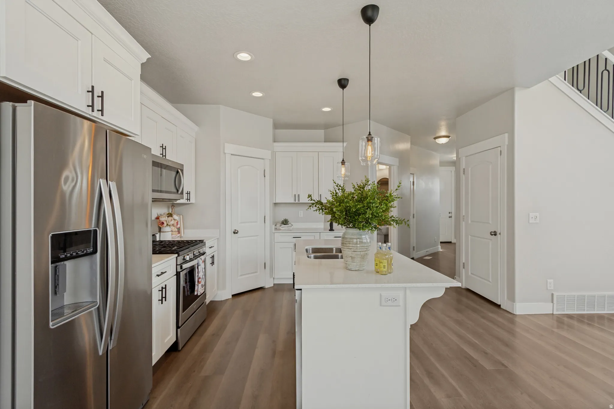 Kitchen featuring white cabinetry, stainless steel appliances, a center island with pendant lighting, and wood-finish flooring.