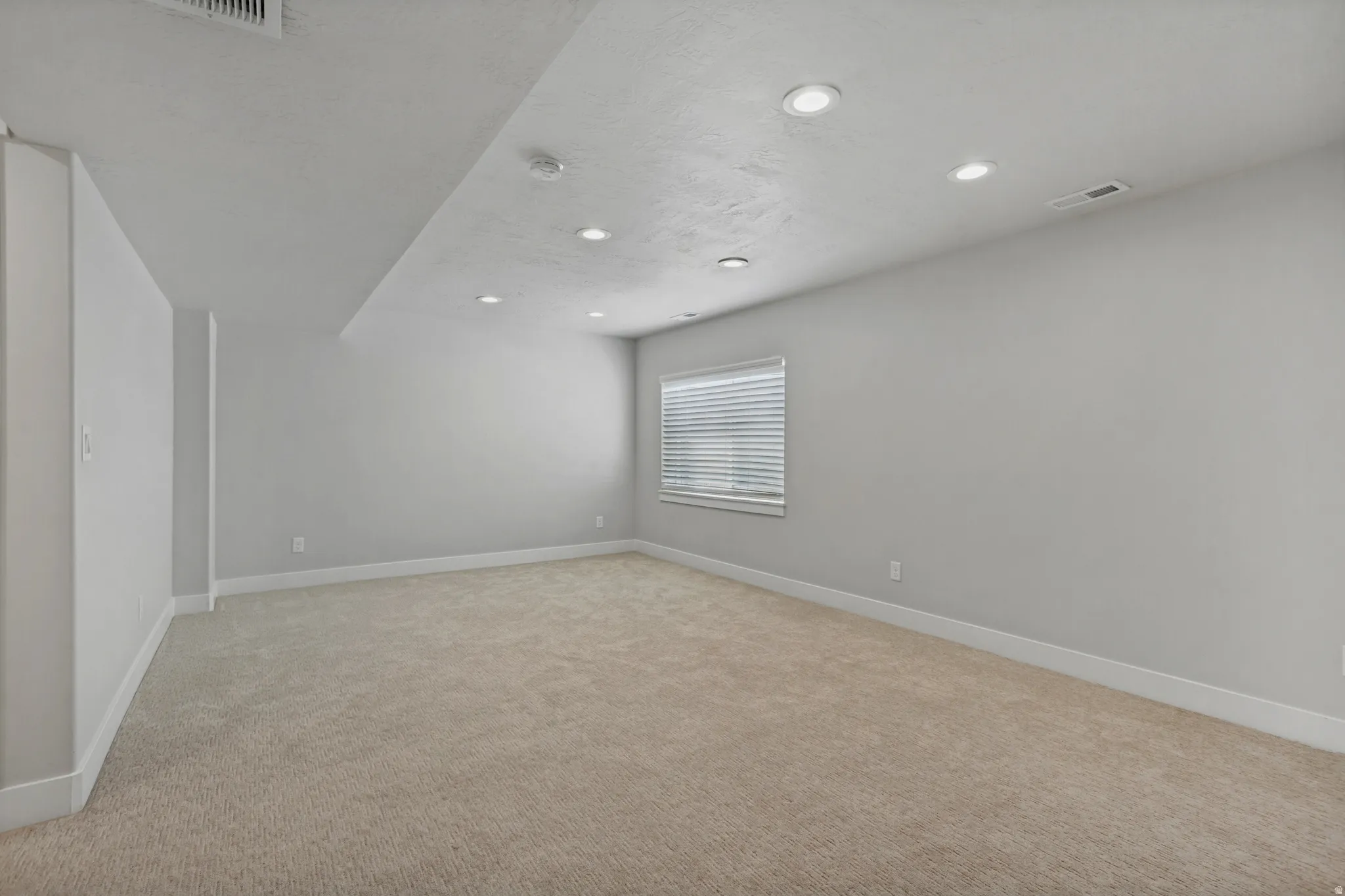 Carpeted room with recessed lighting and a window featuring horizontal blinds.
