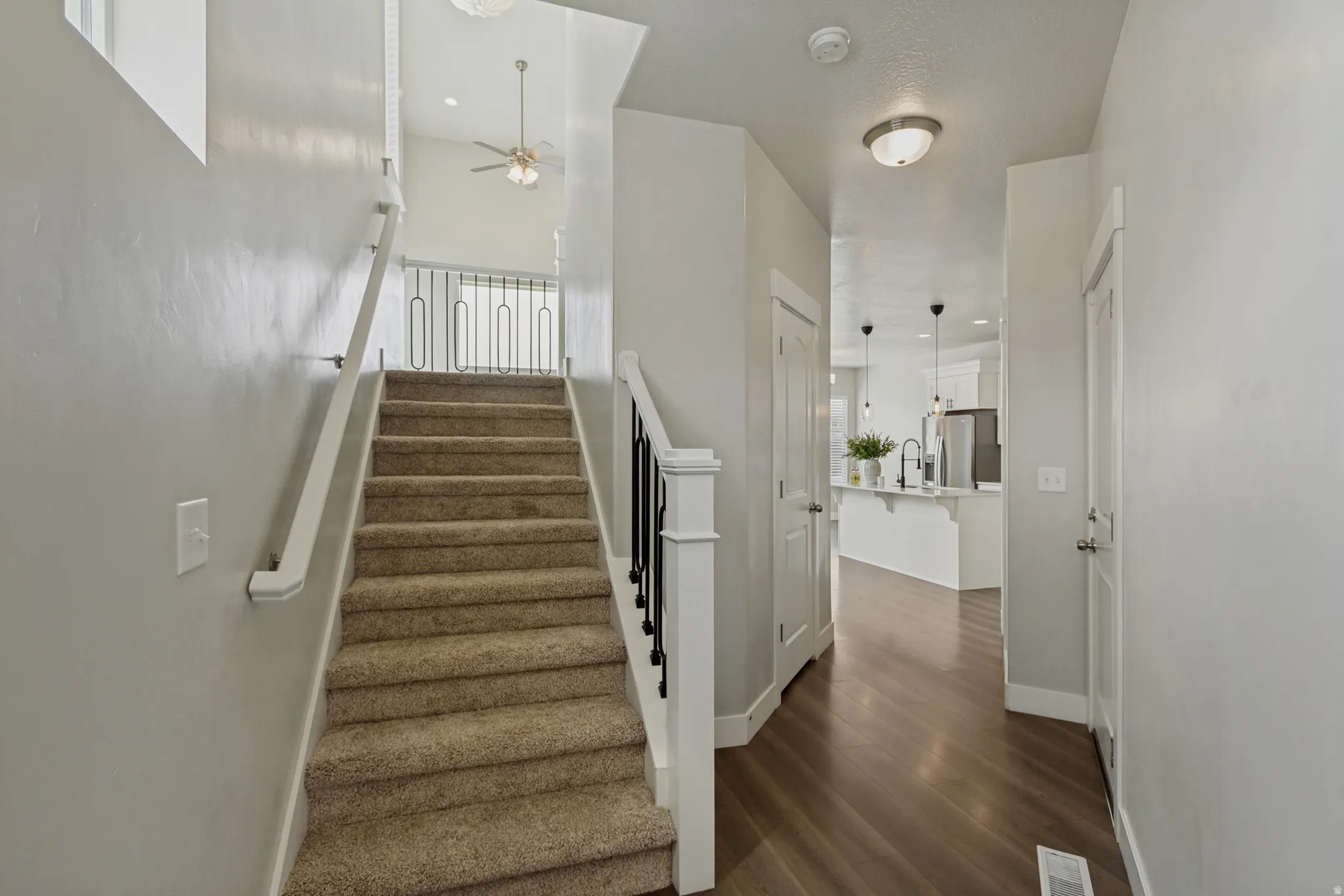 New carpeted staircase with wrought iron balusters, wood-finish flooring, and a kitchen with pendant lighting and an island.