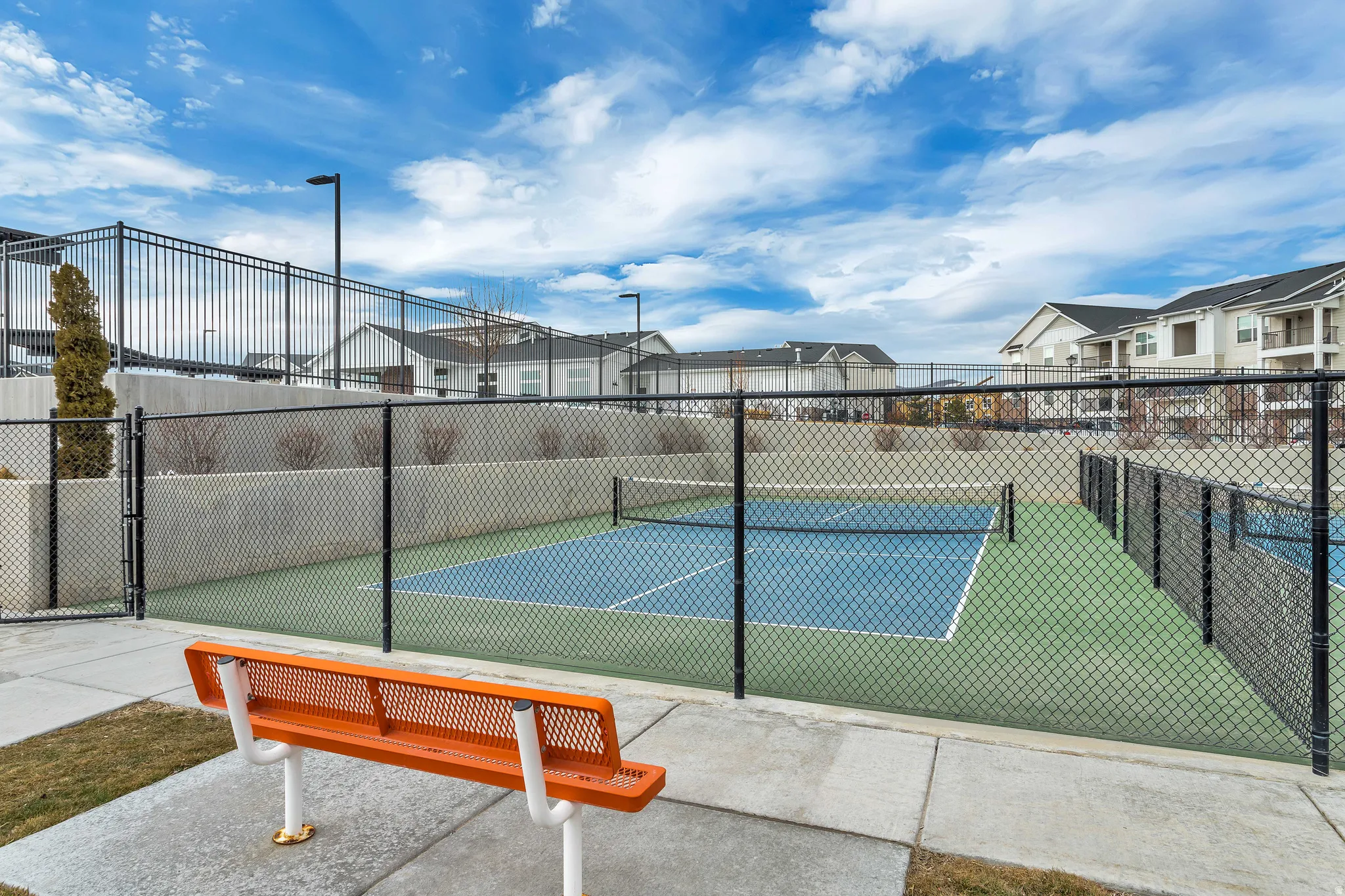 Fenced sports court with blue and green surfacing, surrounded by concrete pathways.