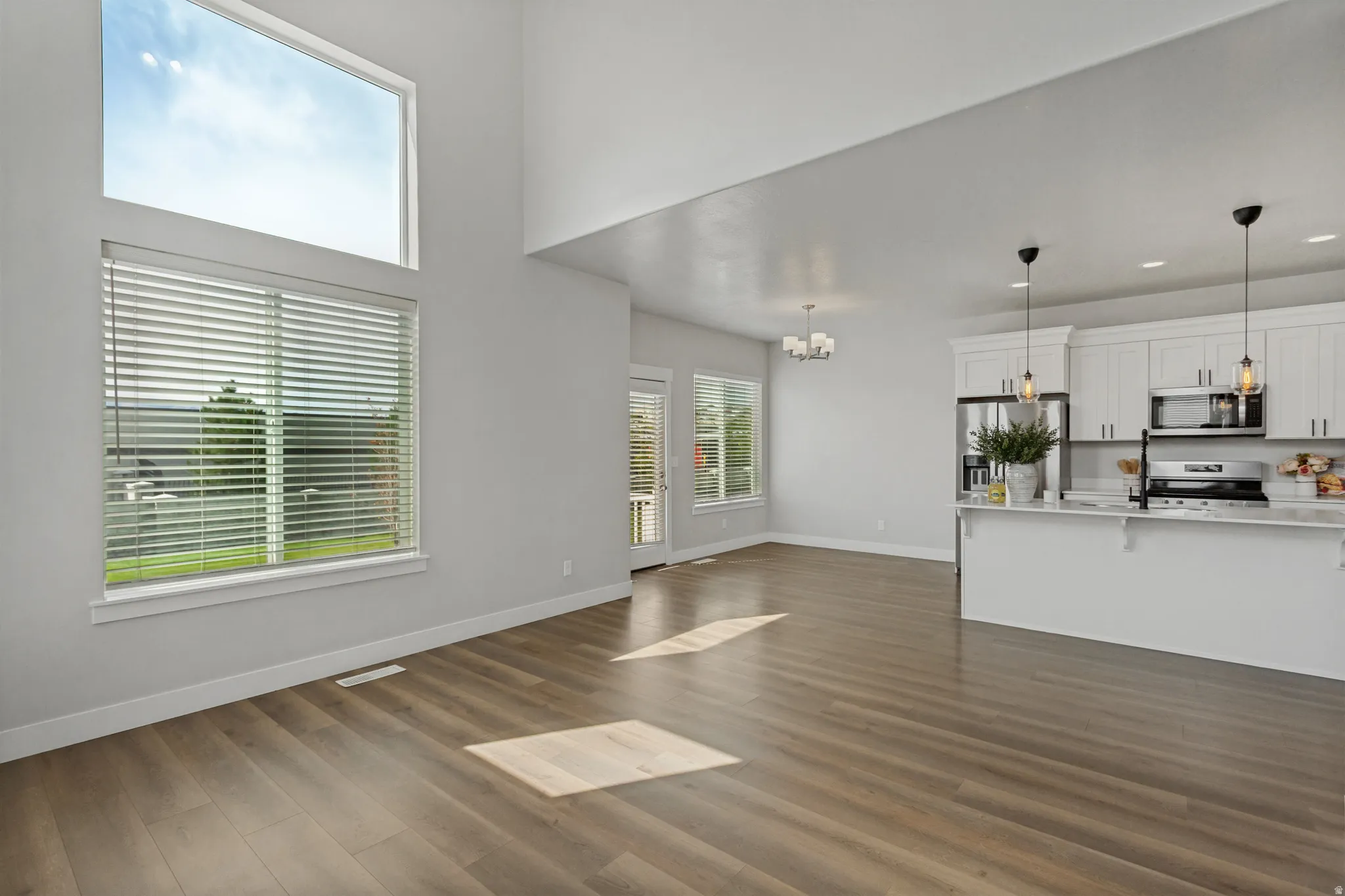 Vaulted ceiling, wood-finish flooring, white cabinetry, stainless steel appliances, and a kitchen island with pendant lighting.