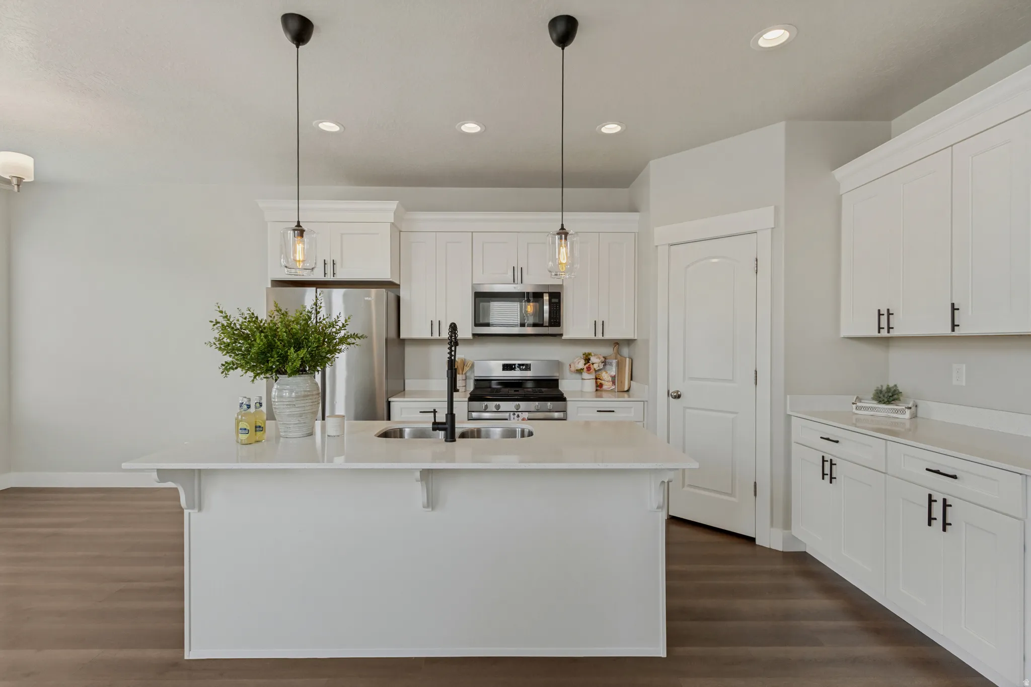 White shaker-style cabinetry with matte black hardware, stainless steel appliances, and a central island with a double basin sink and a walk in pantry.