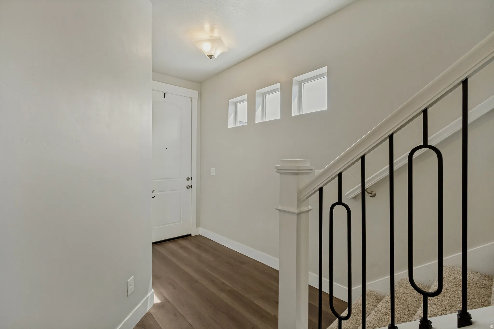 Entryway featuring wood-finish flooring, a white paneled door, and a staircase with a white banister and black metal balusters.