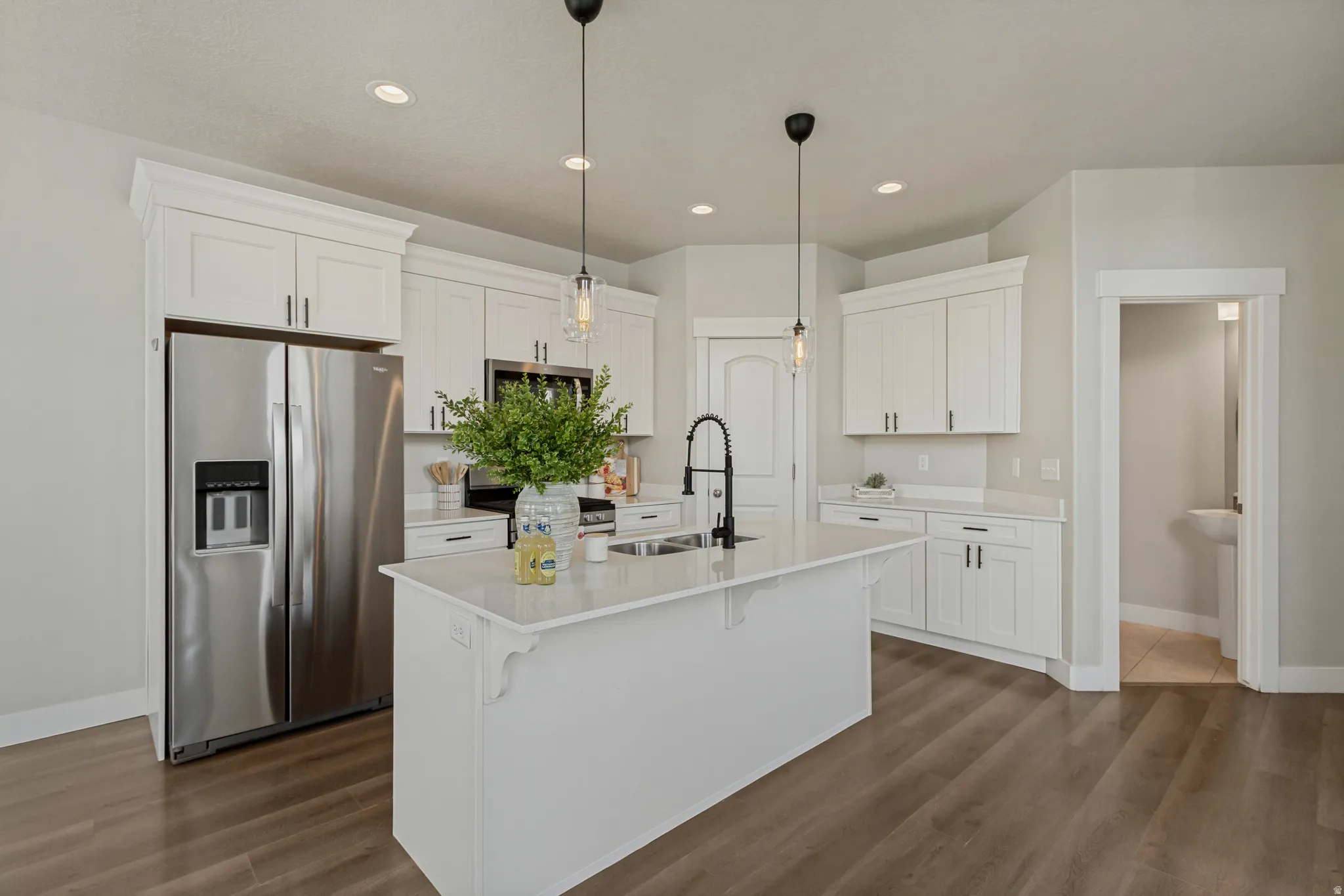 Kitchen featuring white shaker cabinetry, stainless steel appliances, a center island with a sink and pendant lighting, and wood-finish flooring.