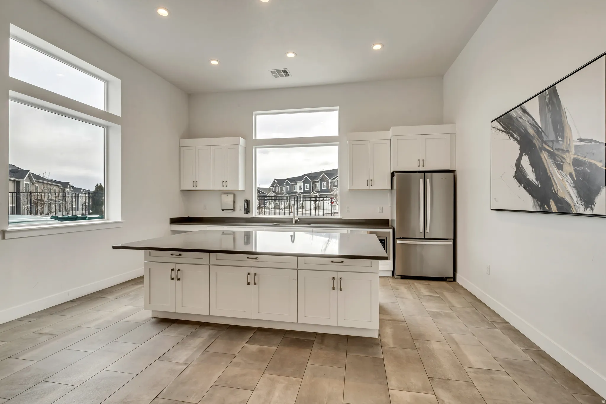 Clubhouse kitchen featuring a large central island, white cabinetry, stainless steel refrigerator, and wood-finish flooring.