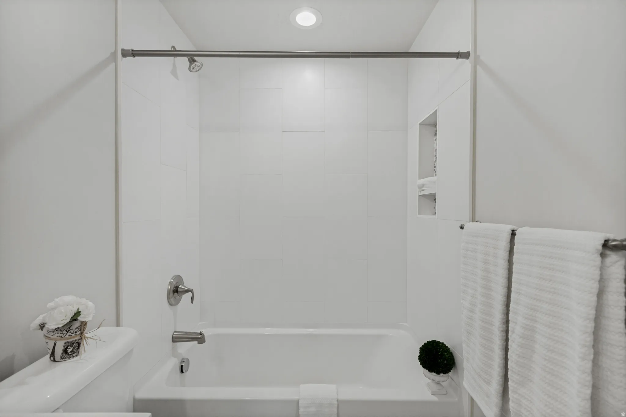 White subway tile shower surround, recessed shower niche, built-in tub with chrome fixtures, and overhead recessed lighting.