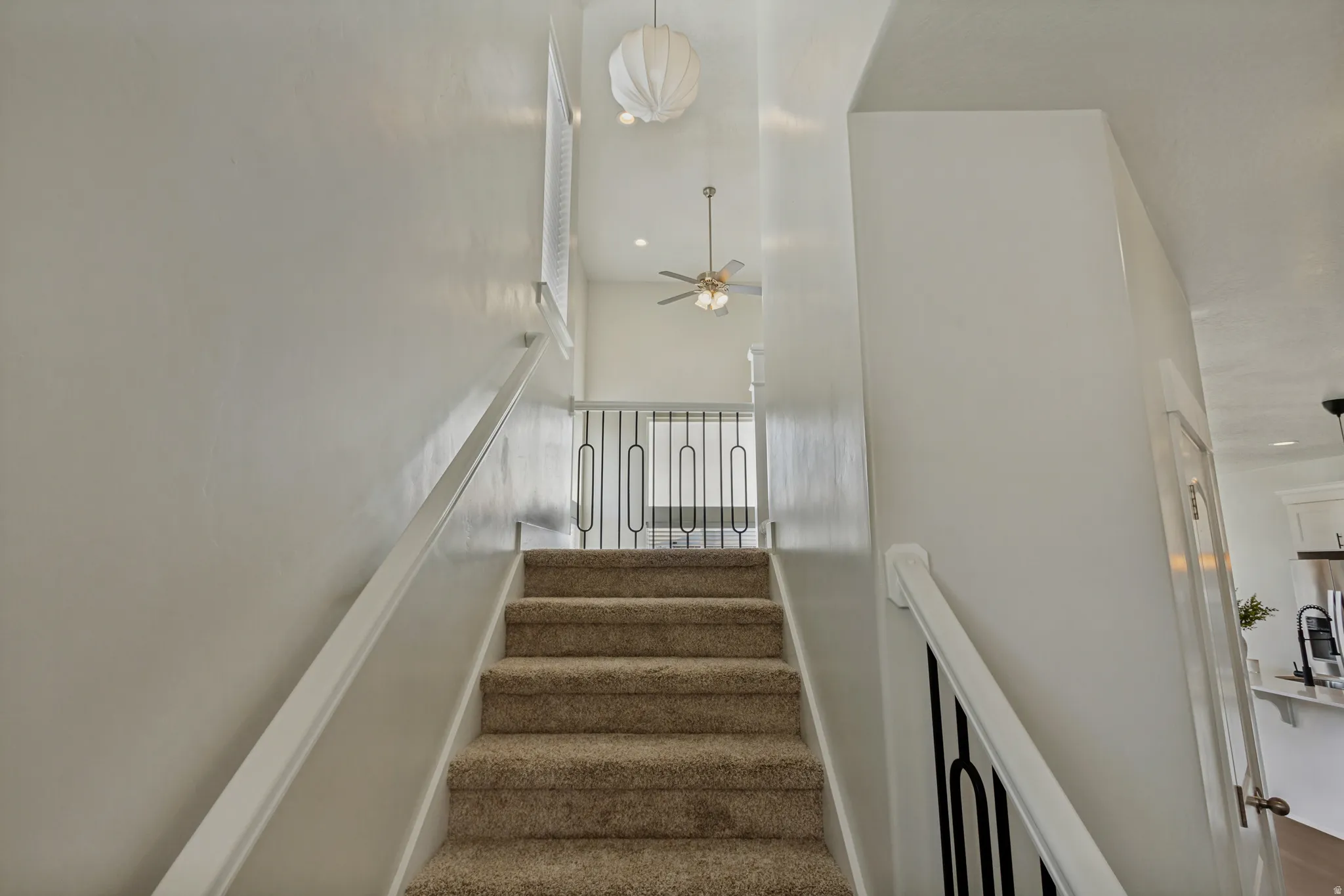 Staircase featuring new carpeted treads, white handrails, and decorative metal balusters and upgraded lighting.