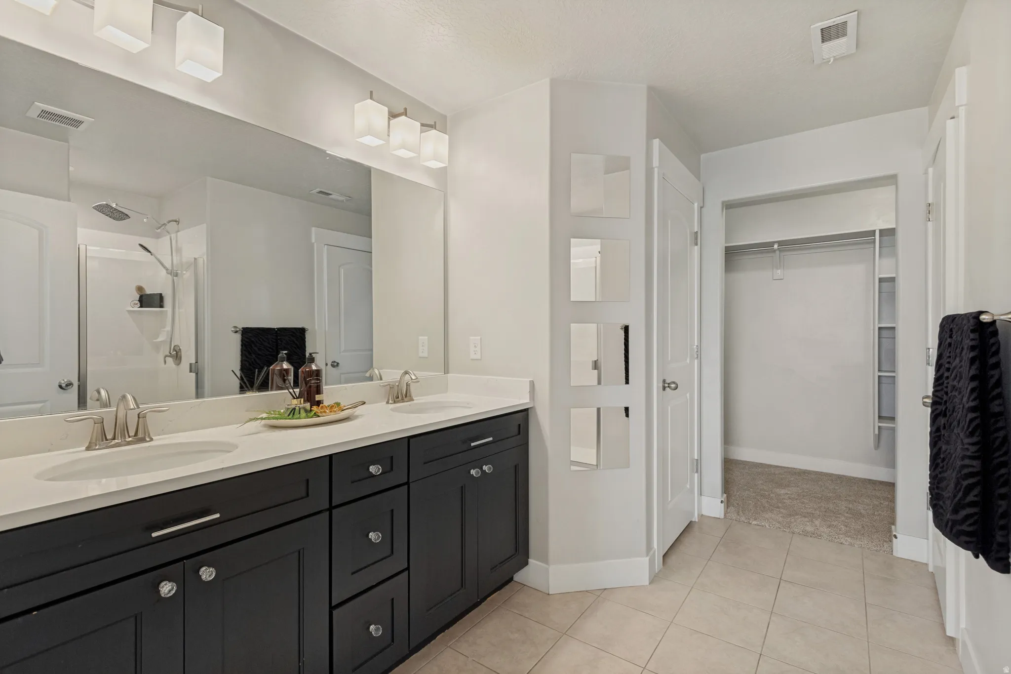 Owners suite bathroom, with double vanity with undermount sinks, stone-finish countertop, and dark wood-finish cabinetry and a large walk-in closet.
