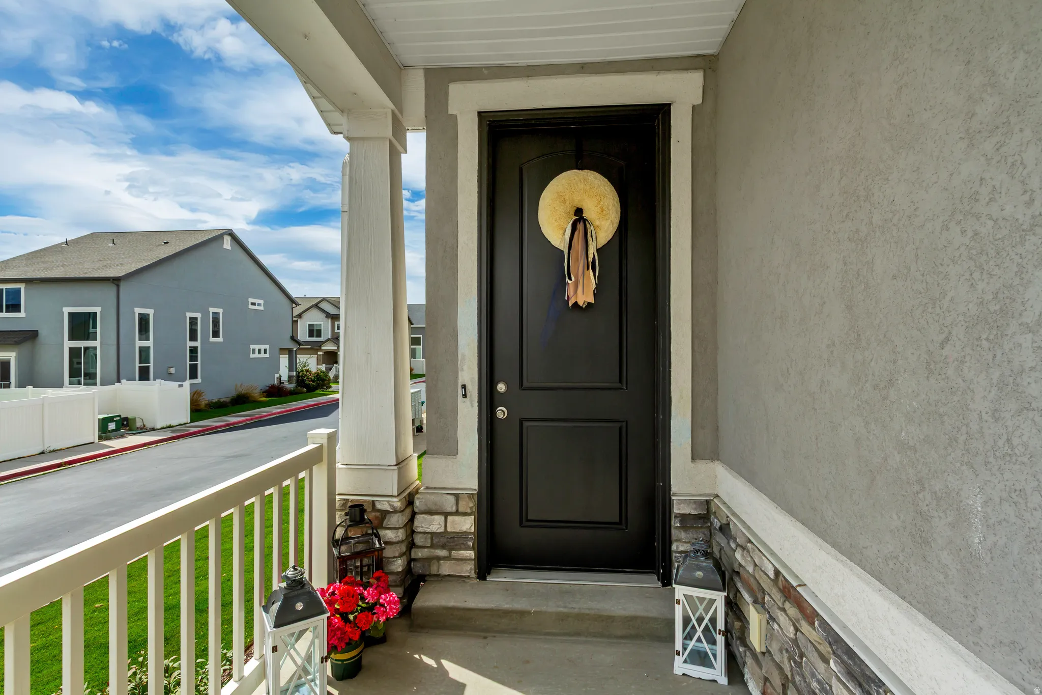 Welcoming front entry featuring a black two-panel door with sidelights, stone and stucco exterior accents, horizontal railings, and a covered porch with white columns and ceiling.