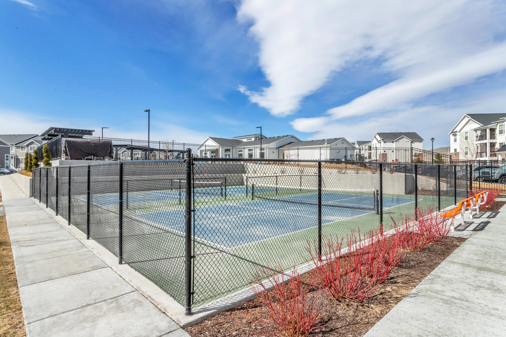 Fenced multi-sport court with a concrete surround, featuring two-tone playing surface and courtside seating.
