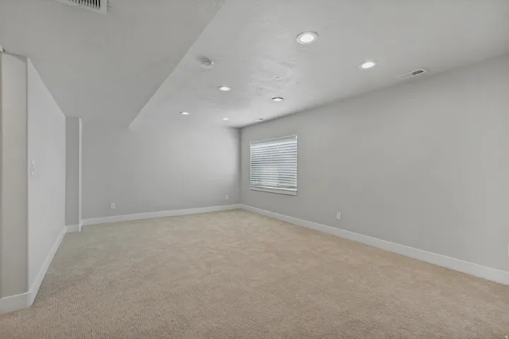 Carpeted room with recessed lighting and a window featuring horizontal blinds.