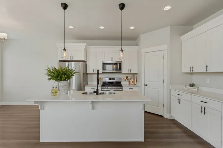 White shaker-style cabinetry with matte black hardware, stainless steel appliances, and a central island with a double basin sink and a walk in pantry.