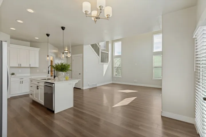 Open-concept living space with wood-finish flooring, a white kitchen island featuring a sink and a new dishwasher, white cabinetry, and multiple tall windows with lots of natural light.