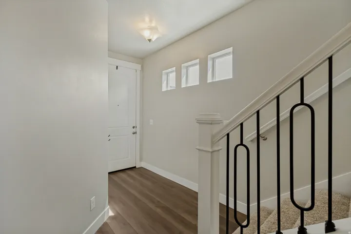 Entryway featuring wood-finish flooring, a white paneled door, and a staircase with a white banister and black metal balusters.