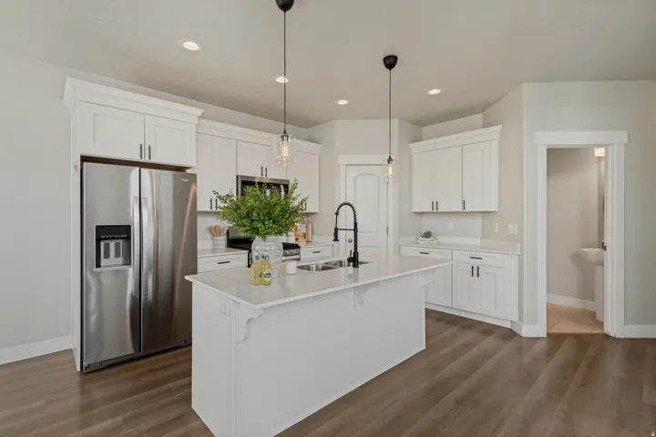 Kitchen featuring white shaker cabinetry, stainless steel appliances, a center island with a sink and pendant lighting, and wood-finish flooring.
