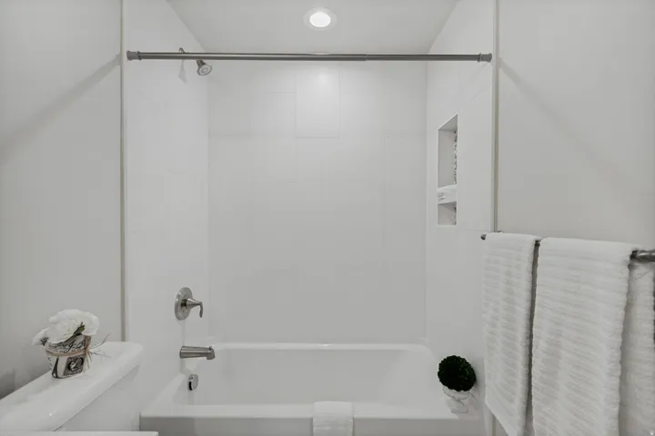 White subway tile shower surround, recessed shower niche, built-in tub with chrome fixtures, and overhead recessed lighting.