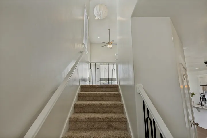 Staircase featuring new carpeted treads, white handrails, and decorative metal balusters and upgraded lighting.