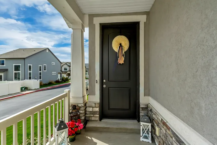 Welcoming front entry featuring a black two-panel door with sidelights, stone and stucco exterior accents, horizontal railings, and a covered porch with white columns and ceiling.