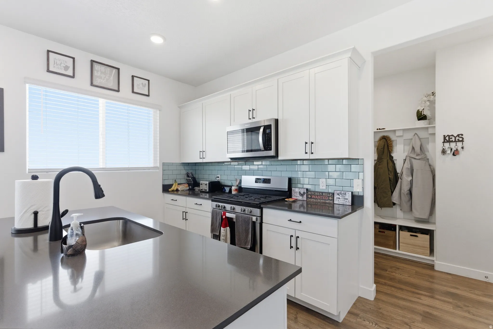 Kitchen featuring white cabinetry, subway tile backsplash, stainless steel appliances, and a central island with an undermount sink