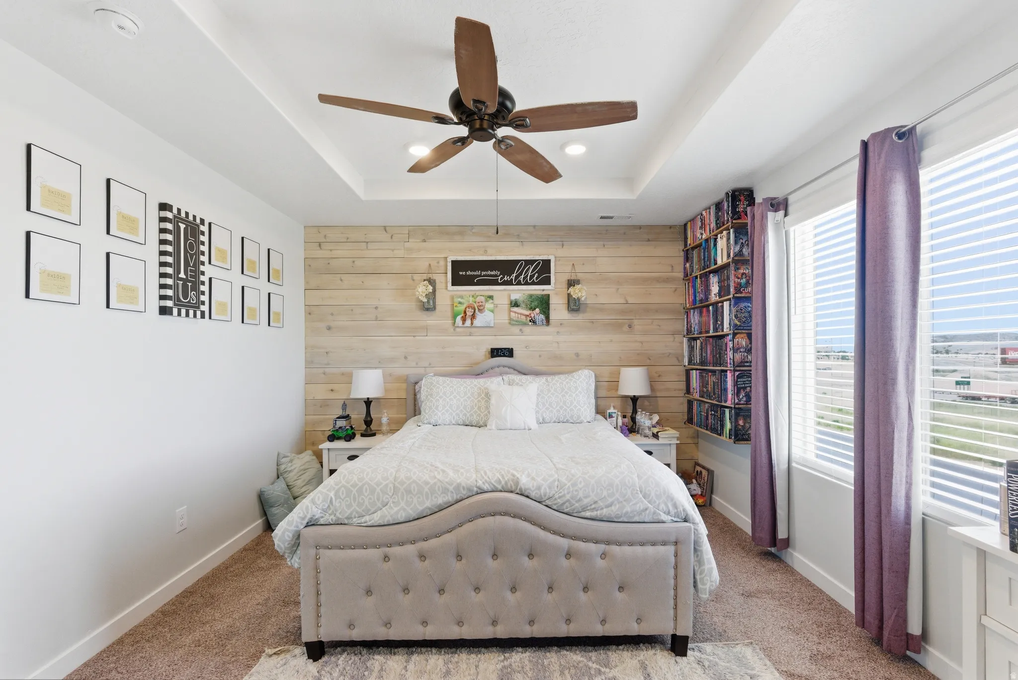 Tray ceiling with a ceiling fan, accent shiplap wall, and built-in shelving