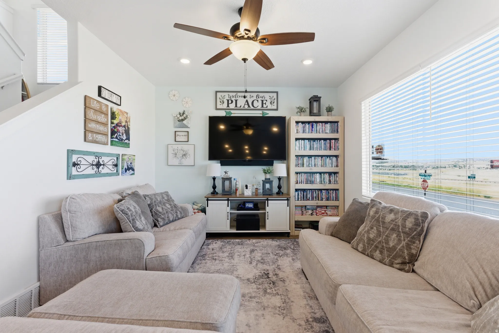 Spacious living area featuring a ceiling fan, recessed lighting, large window with blinds, and wood-finish media console