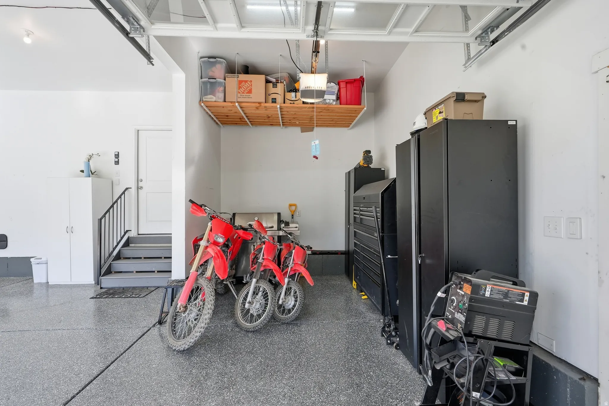 Garage space featuring a speckled epoxy floor, white walls, and an overhead storage shelf