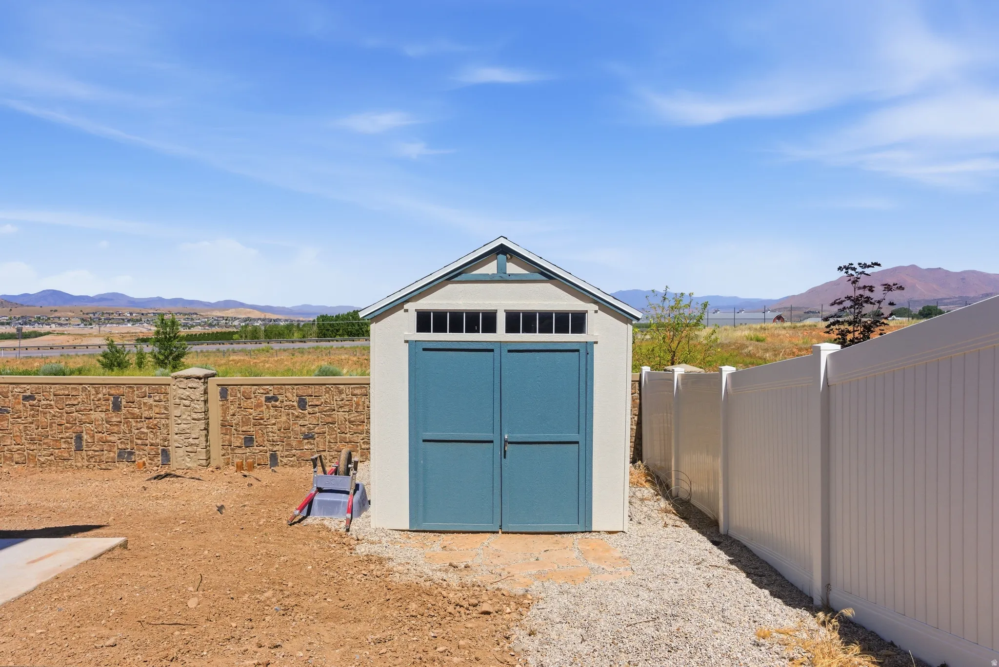 White storage shed with blue double doors, transom windows, and white trim