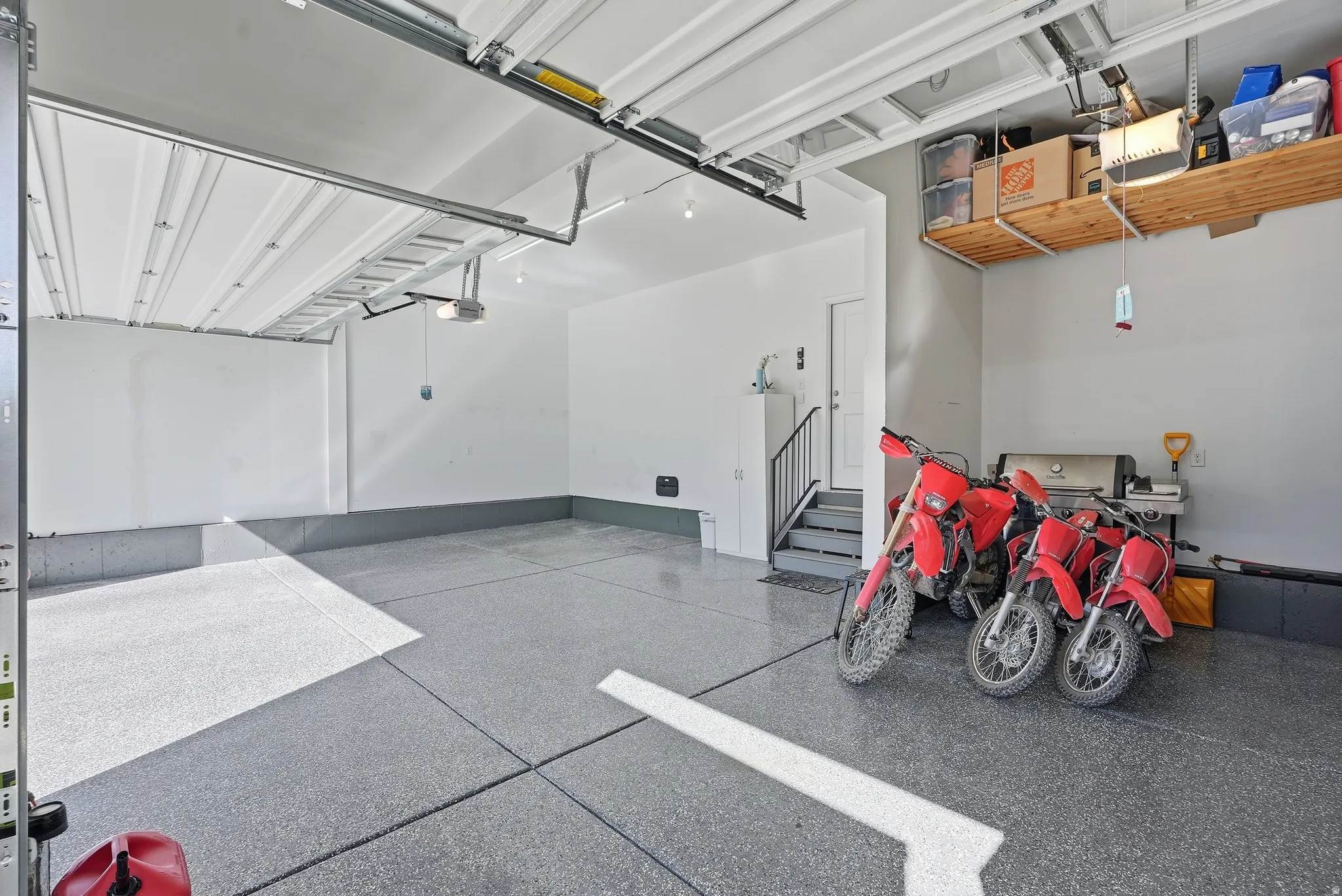 Spacious garage featuring a durable epoxy floor, overhead door, built-in shelving, and interior access stairs