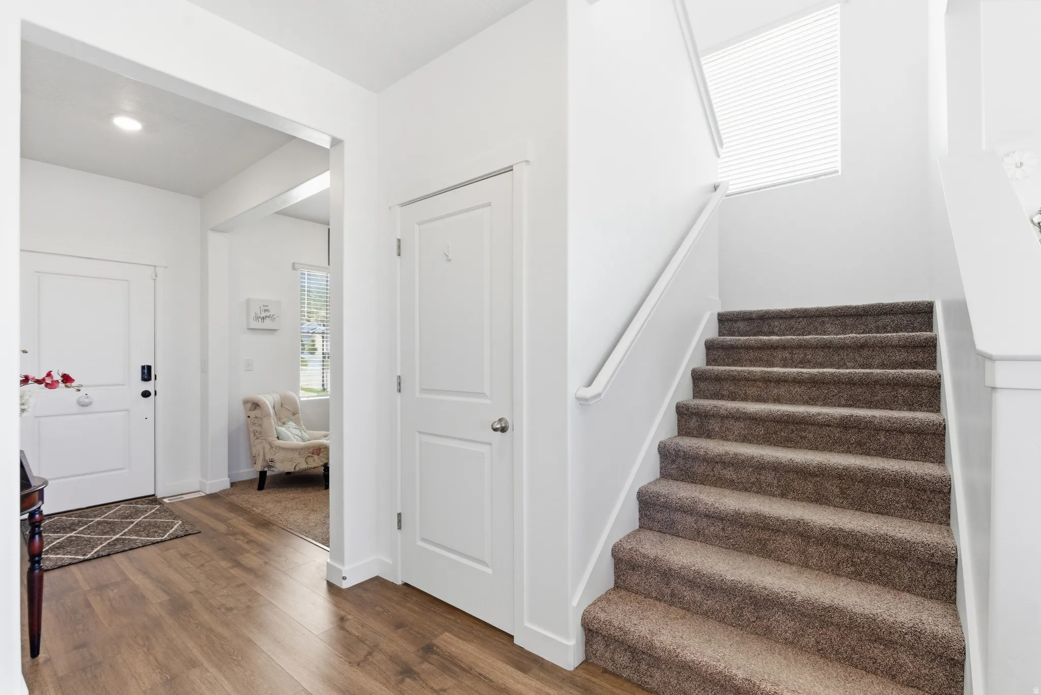 Wood-finish flooring, white paneled doors, staircase with carpeted treads, and a white handrail