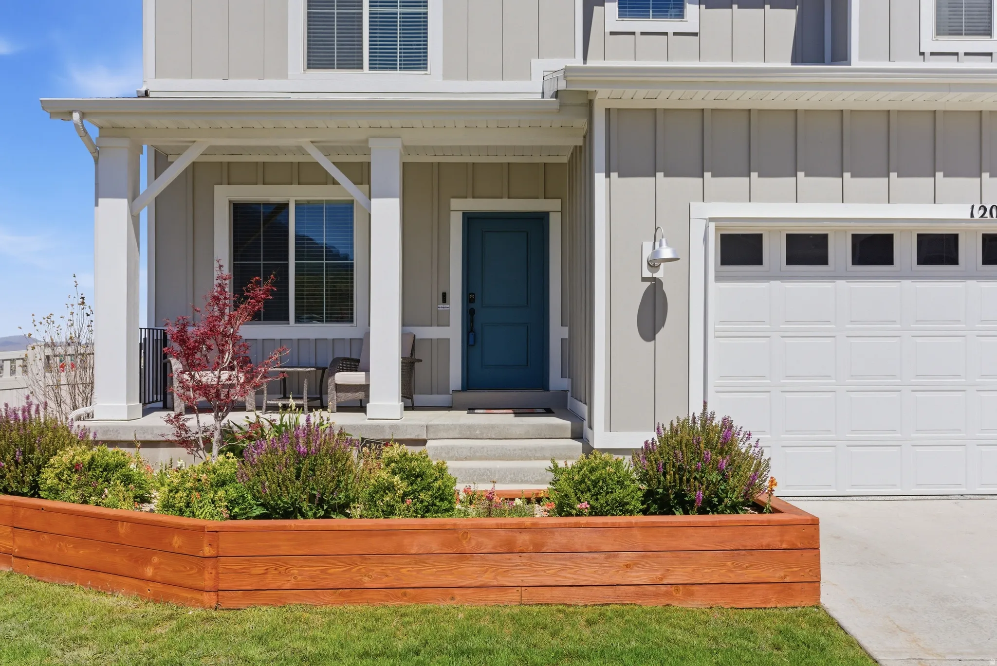 Board and batten exterior with covered porch, wood-finish raised planter, teal front door, and attached garage
