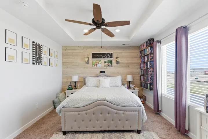 Tray ceiling with a ceiling fan, accent shiplap wall, and built-in shelving