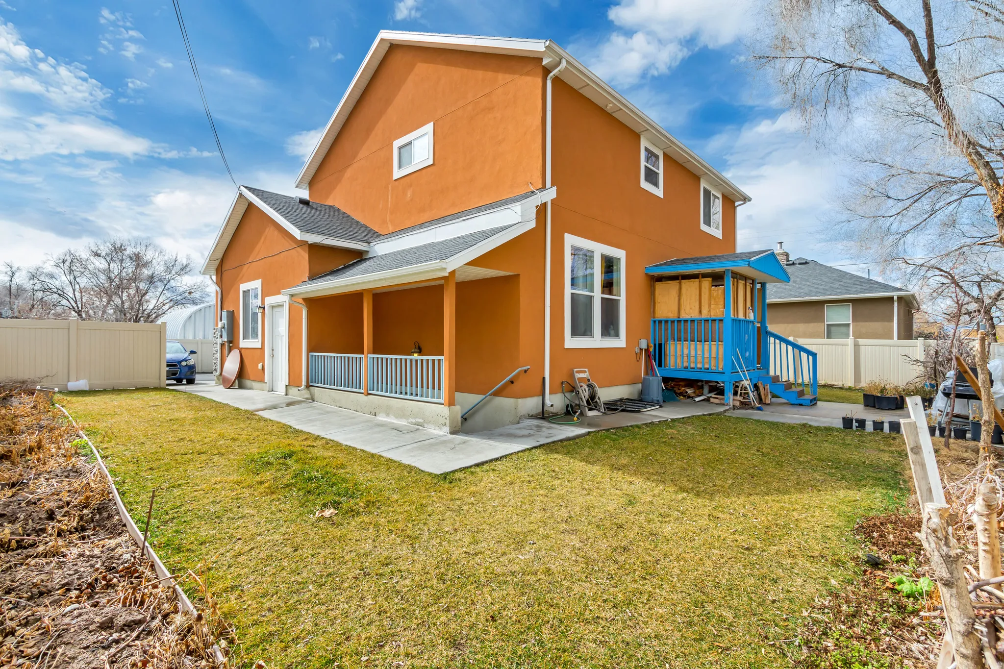 Orange stucco exterior featuring a covered porch, an additional covered entry with blue railing, a concrete patio, and a grassy lawn area