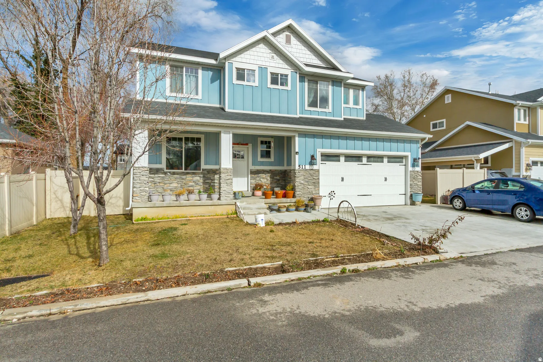Two-story residence featuring light blue siding, white trim, stone veneer accents, a covered porch, and an attached two-car garage
