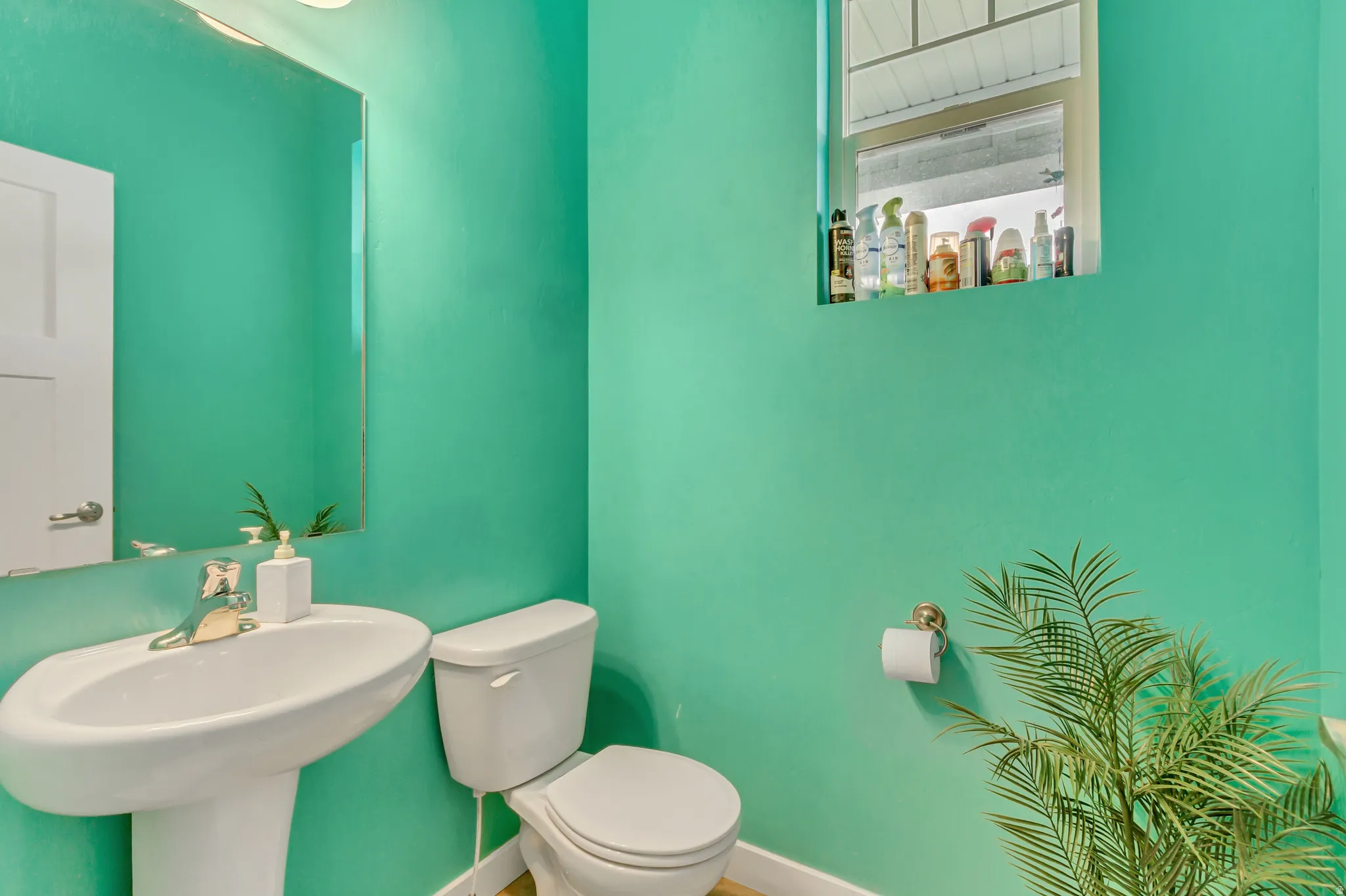 Pedestal sink with chrome faucet, wall-mounted mirror, toilet, and a window with a sill