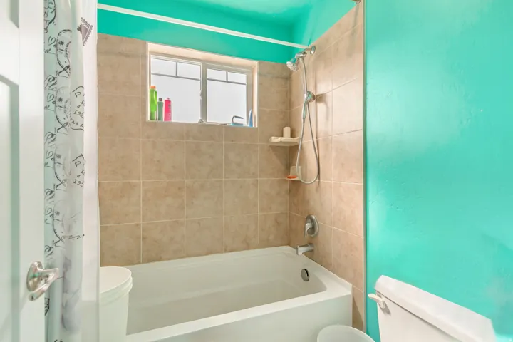 Bathtub with tile surround, shower fixture with handheld spray, and a window for natural light