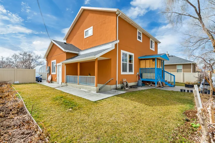Orange stucco exterior featuring a covered porch, an additional covered entry with blue railing, a concrete patio, and a grassy lawn area