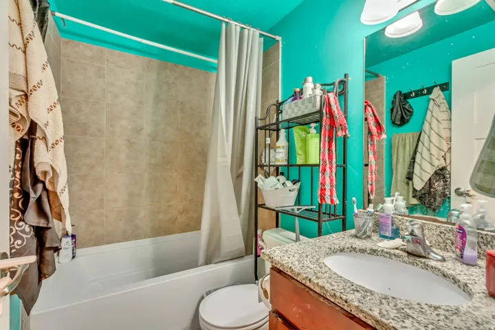 Bathroom featuring a single vanity with stone-look countertop, integrated sink, and tile-surround bathtub