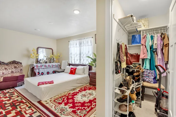 Recessed ceiling lighting, light-toned wall paint, window with sheer curtains, and a built-in closet with shelving and hanging rods