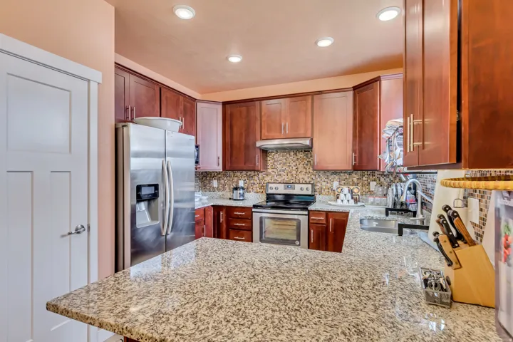 Kitchen featuring granite countertops, stainless steel appliances, wood cabinetry, recessed lighting, and a mosaic tile backsplash