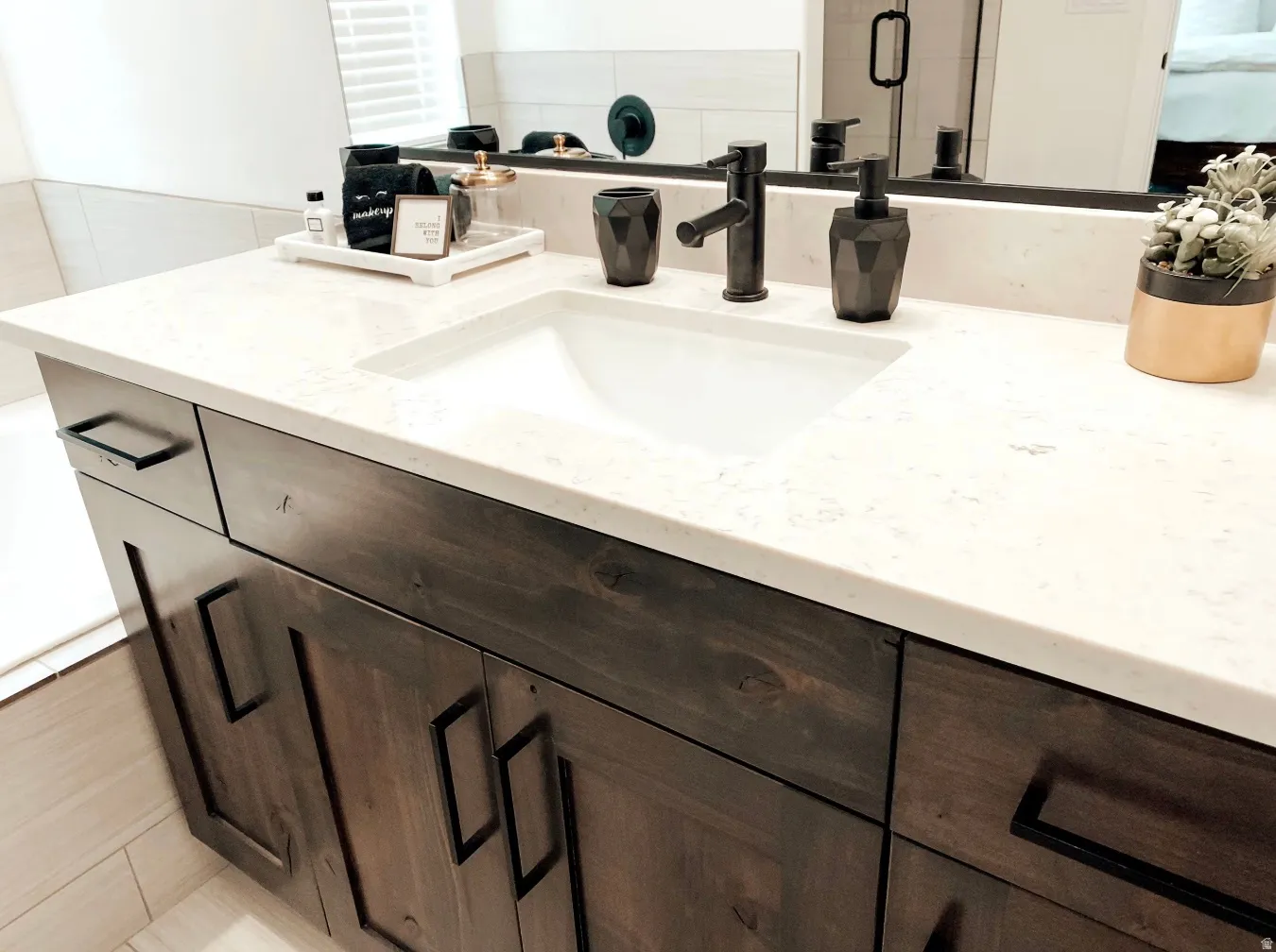 Vanity featuring a single undermount sink, light-toned countertop, dark wood-finish cabinetry, and matte black hardware
