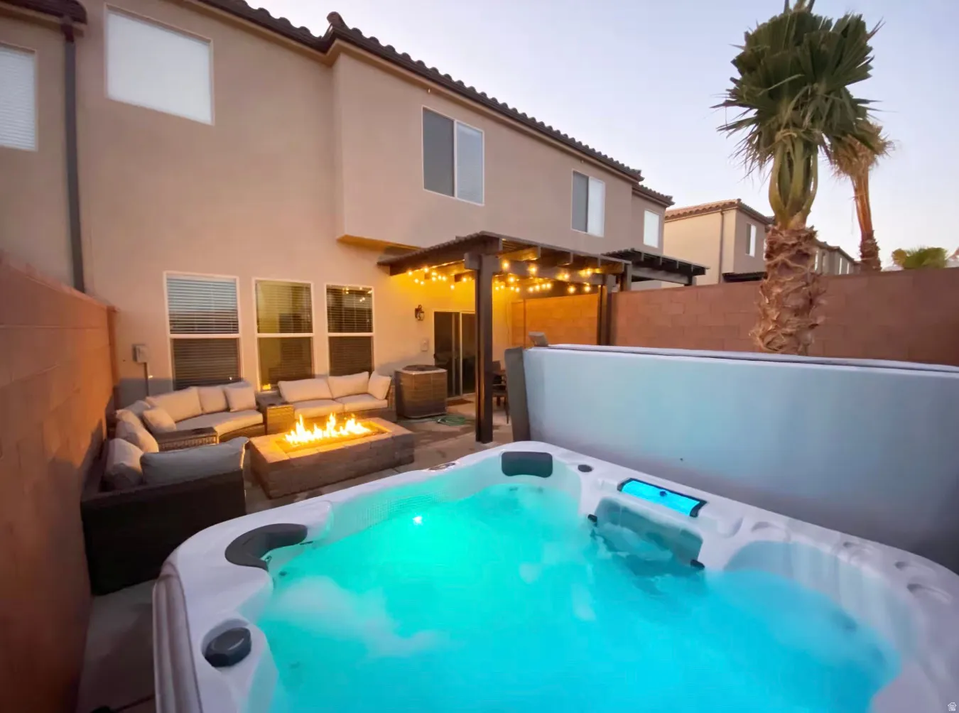 Backyard featuring a built-in spa, fire pit, string lighting, and a stucco exterior