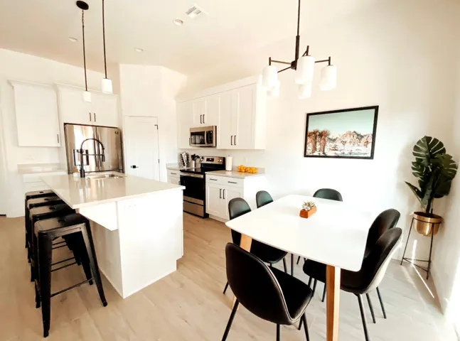 White kitchen cabinetry with stainless steel appliances, central island with integrated sink, pendant lighting, and wood-finish flooring
