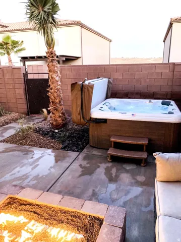 Outdoor patio featuring a hot tub, stone-edged fire pit, concrete pavers, and a mature palm tree