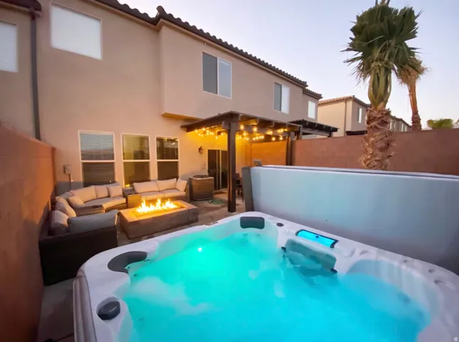 Backyard featuring a built-in spa, fire pit, string lighting, and a stucco exterior