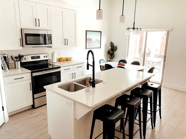 Kitchen featuring white cabinetry, stainless steel appliances, a center island with dual sinks, and wood-finish flooring