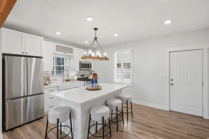 White shaker cabinetry, stainless steel appliances, central kitchen island with seating, wood-finish flooring, and recessed lighting