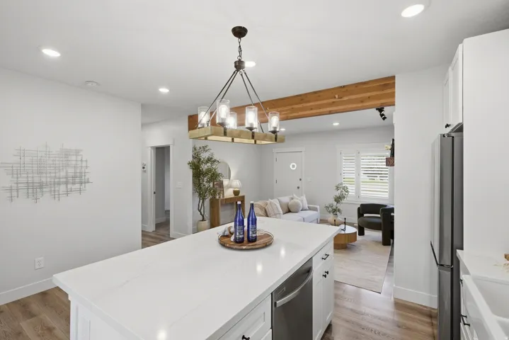 White kitchen island with a built-in dishwasher, recessed lighting, exposed wood beam, and a contemporary chandelier