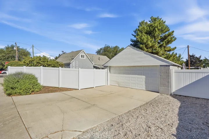 Detached 2 garage with a paneled door, concrete driveway, and white privacy fencing