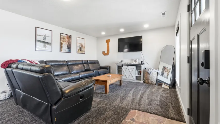 Recessed ceiling lighting, dark paneled entry door, white trim, carpeted flooring, and a white entertainment console
