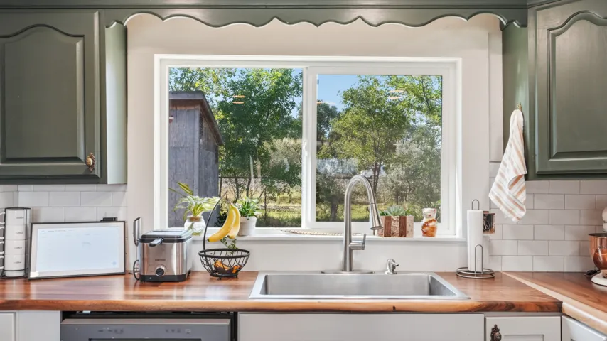 Wood-finish countertops, subway tile backsplash, stainless steel sink, pull-down faucet, and painted cabinetry